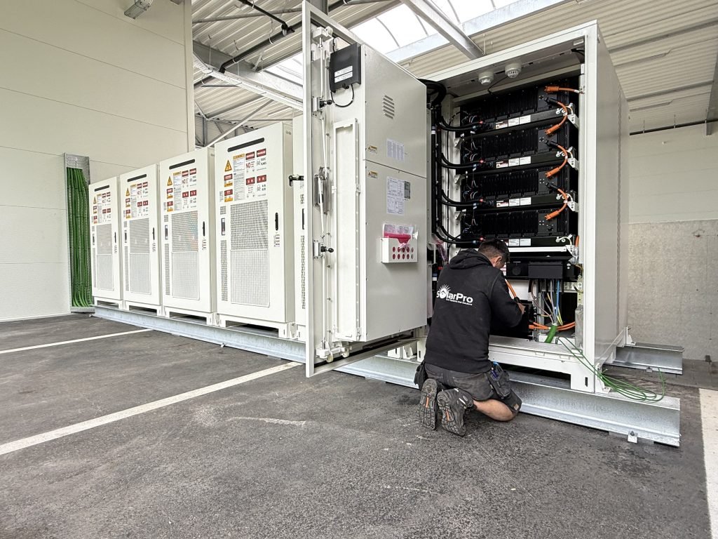 Monteur werkt aan de aansluiting van een industriële batterijopslaginstallatie in een technische ruimte.